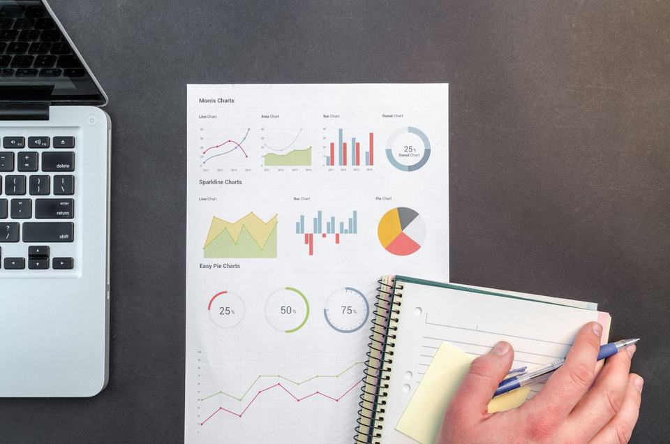 A laptop, printed charts, and a notebook on a desk.