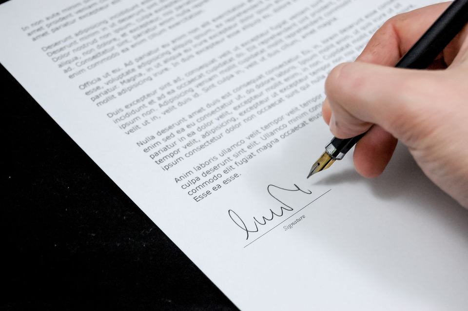 A close view of a hand signing a printed document with a fountain pen.