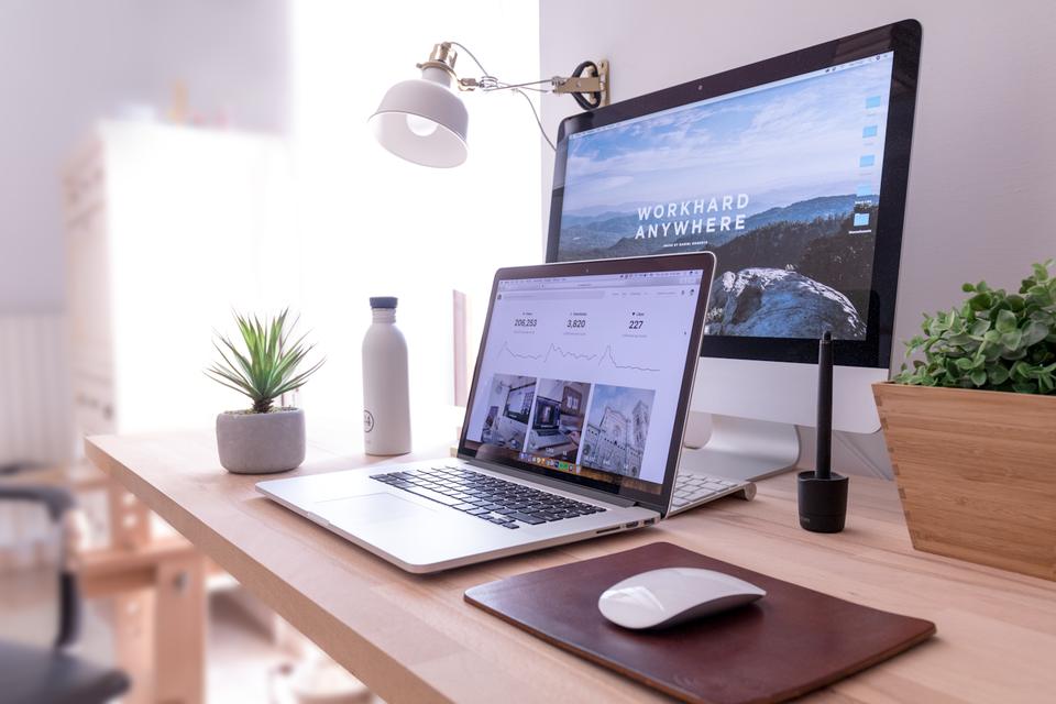 A bright desk with a laptop and desktop monitor showing a website layout.